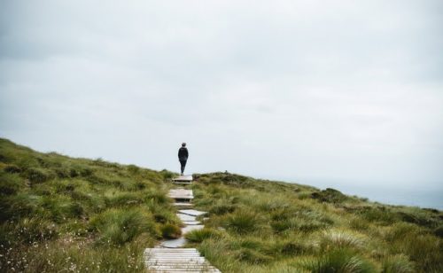 En person står på en sti i naturen, omgitt av grønt landskap og åpen himmel, symboliserer mental helse og personlig vekst i psykoterapi.