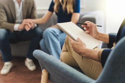 Couple Therapy Insight: Focus on Therapist’s Notebook with Young Married Couple in Background Couple Therapy Insight: Focus on Therapist's Notebook with Young Married Couple in Background